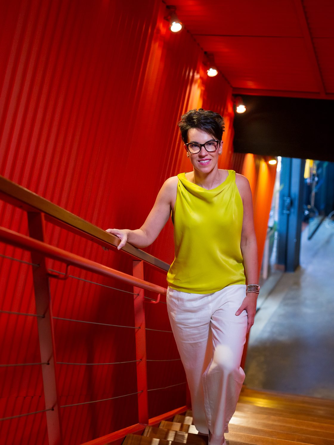 Juliana Pescara saindo fora da caixa, em escadaria de corredor vermelho